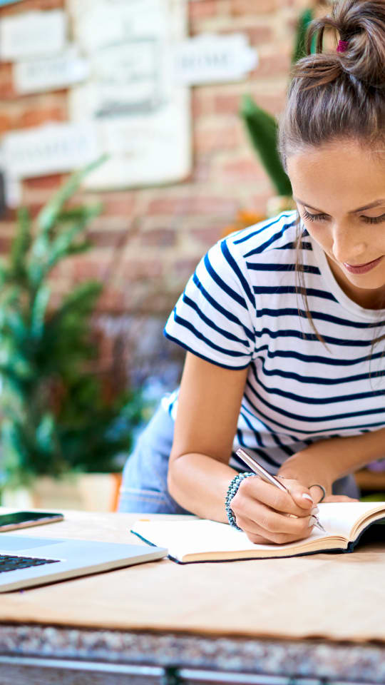 Person writing in notebook with laptop on table